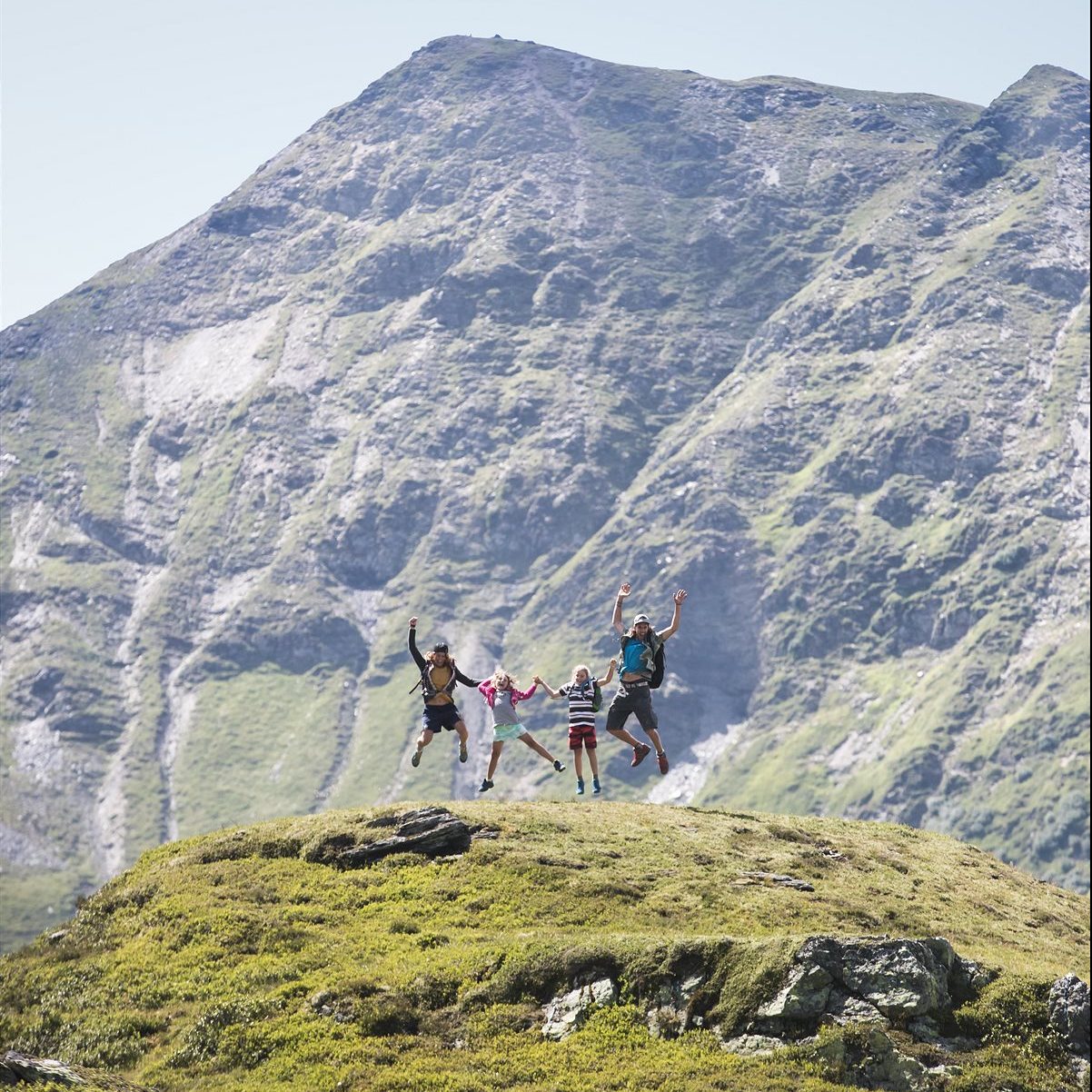Familie springt vor der Bergkulisse von Saalbach im Salzburgerland vor Freude in die Luft